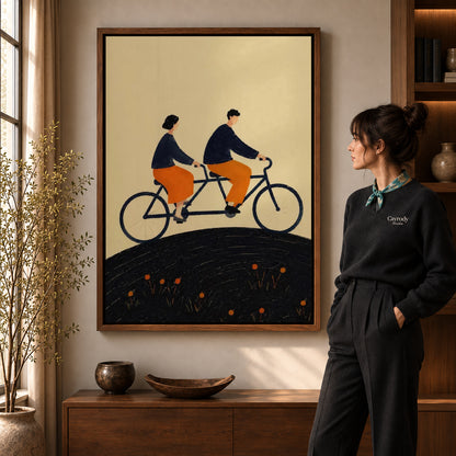 Tandem Ride canvas art in a walnut frame beside a standing woman and wooden console.