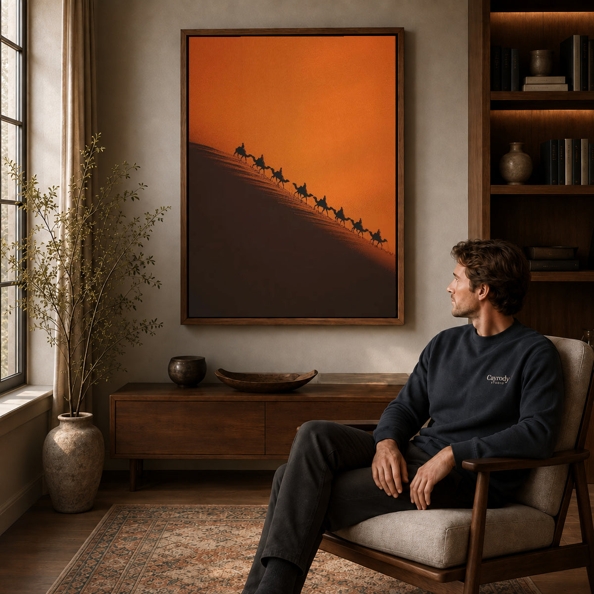 Desert Caravan canvas art above a wooden console beside a seated man in a warm room.