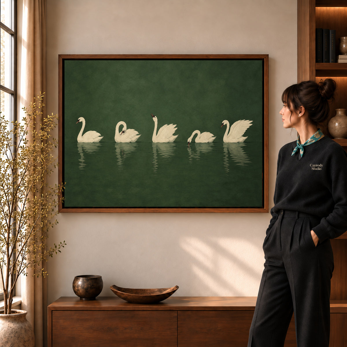 Quiet Swan Gathering canvas art in a walnut frame beside a standing woman and wooden console.