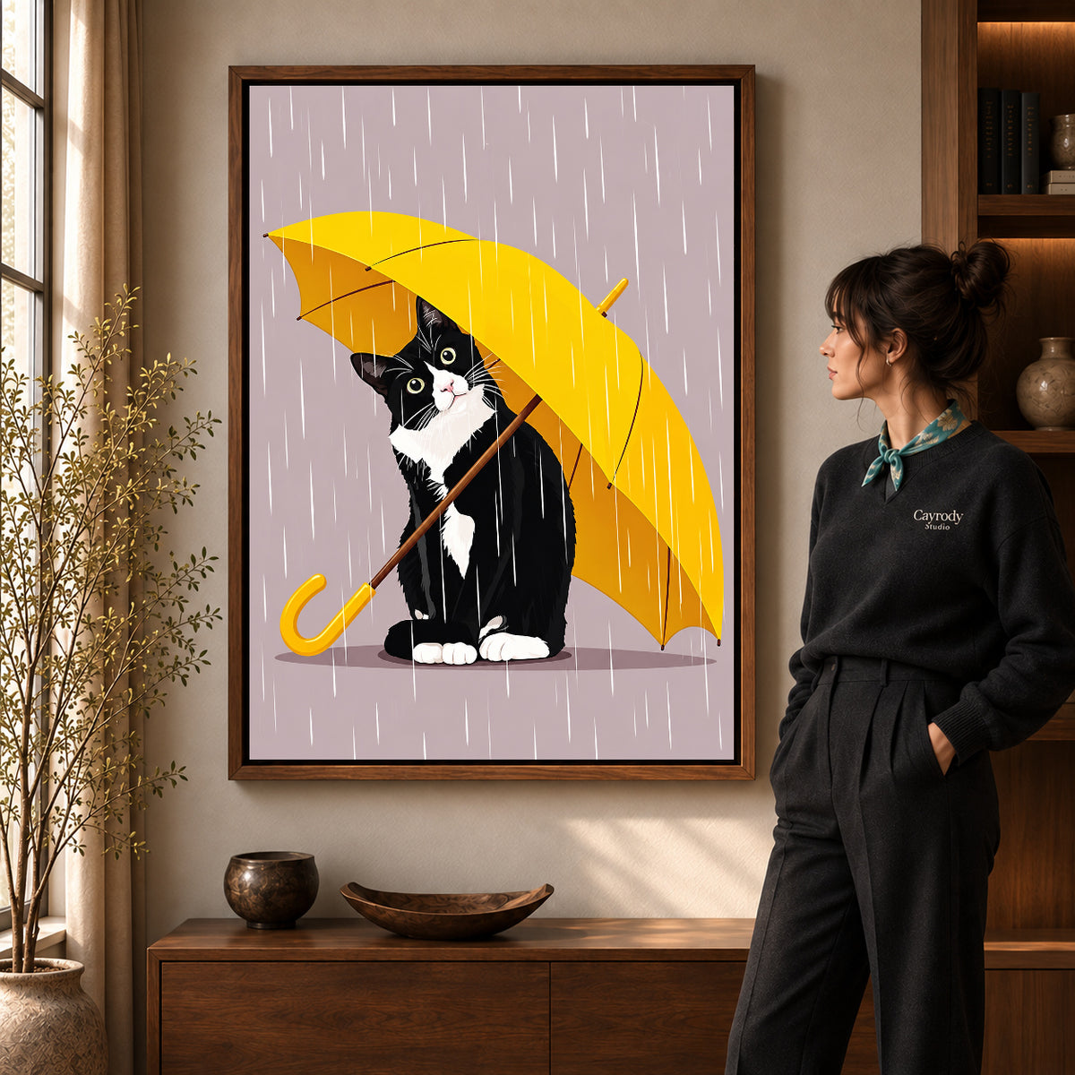 Umbrella Cat Canvas Art in a walnut frame beside a standing woman and warm wooden furniture.