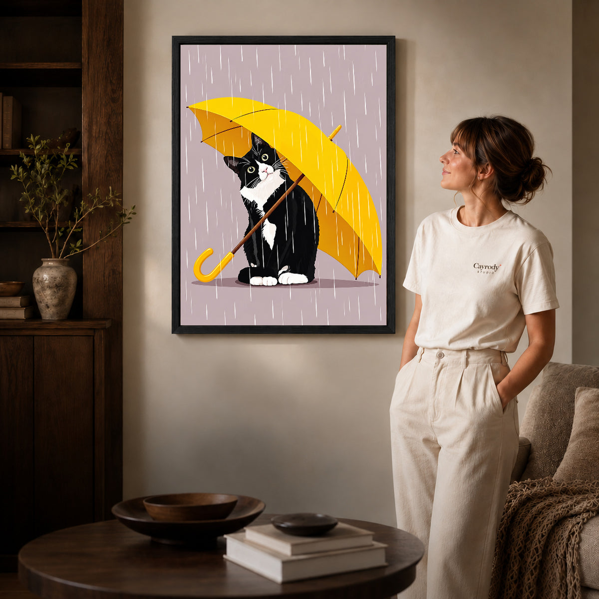 Umbrella Cat Canvas Art inside a black frame in a softly lit living room with books.