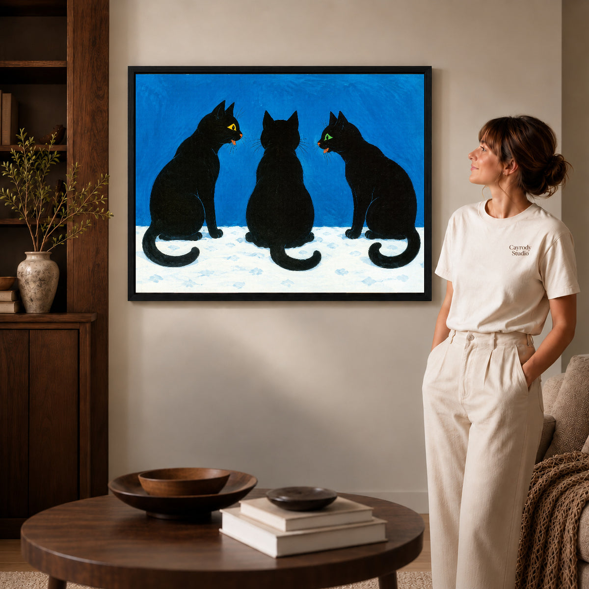 Black Cat Canvas Art inside a black frame in a softly lit living room with books.