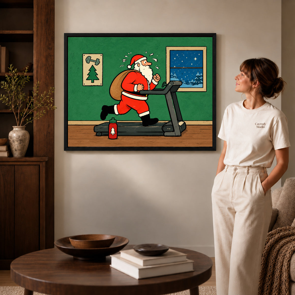 christmas workout santa canvas art in a black frame beside a woman and round wooden table.