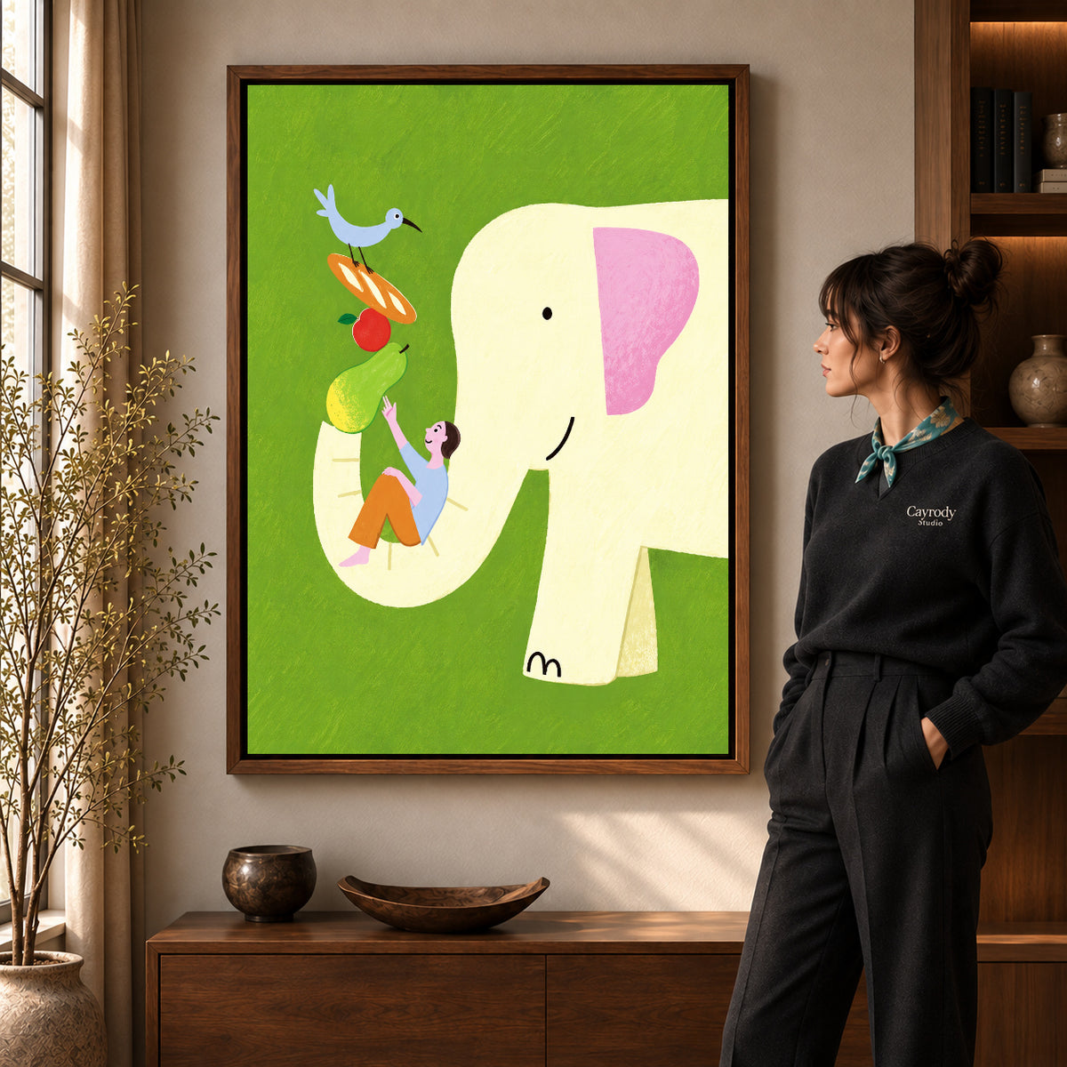 Elephant Canvas Art in a walnut frame beside a standing woman and warm wooden furniture.