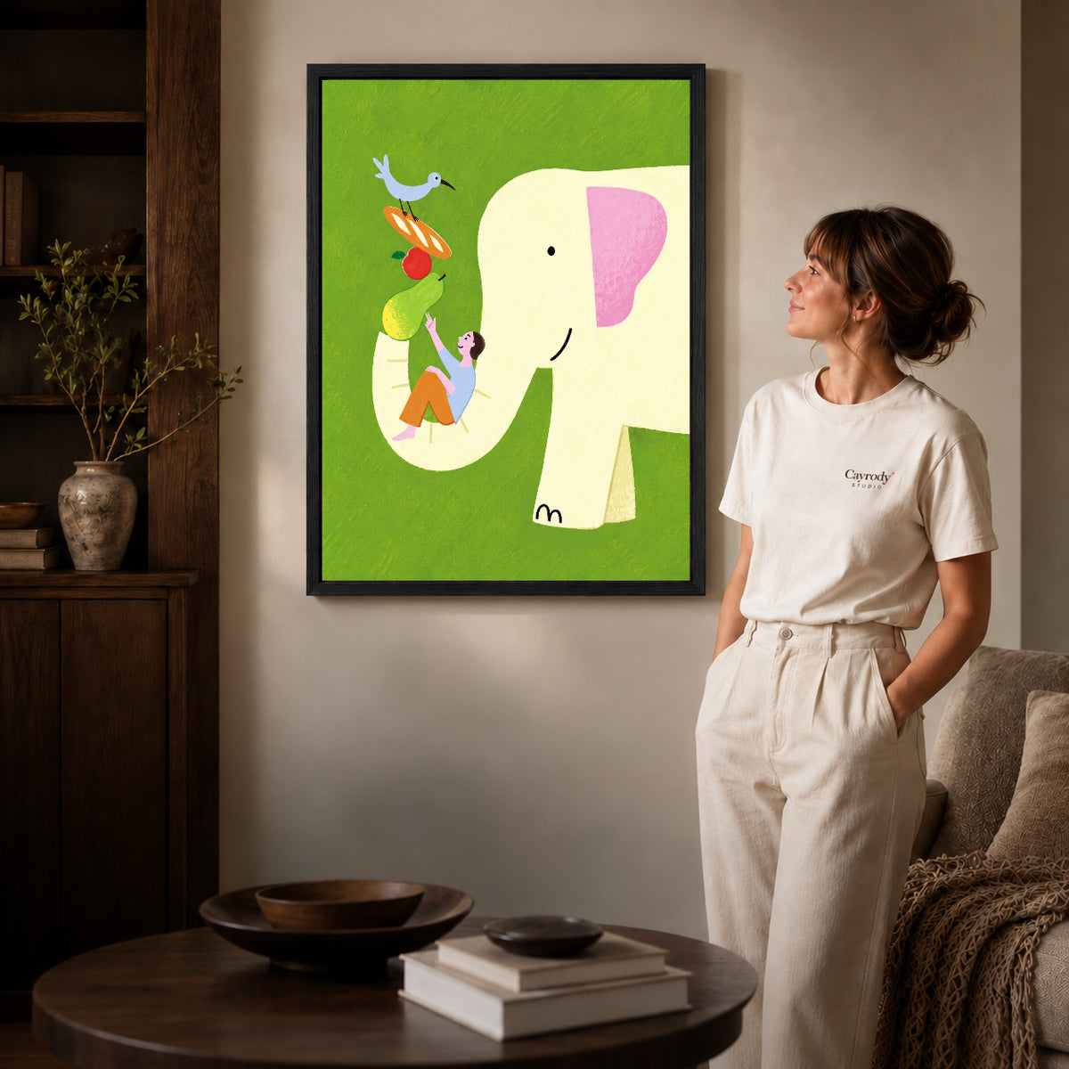 Elephant Canvas Art inside a black frame in a softly lit living room with books.