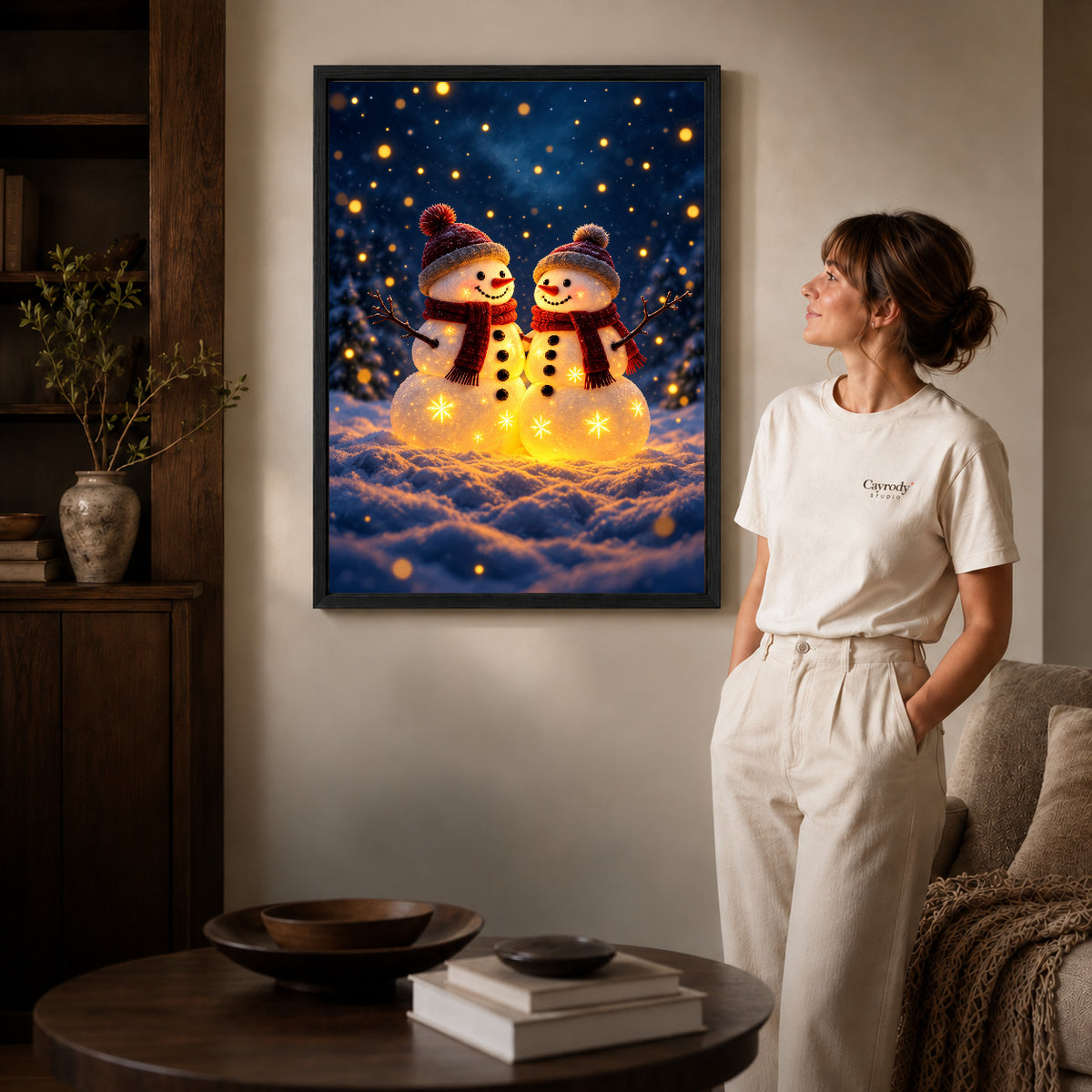 Snowman Canvas Art inside a black frame in a softly lit living room with books.