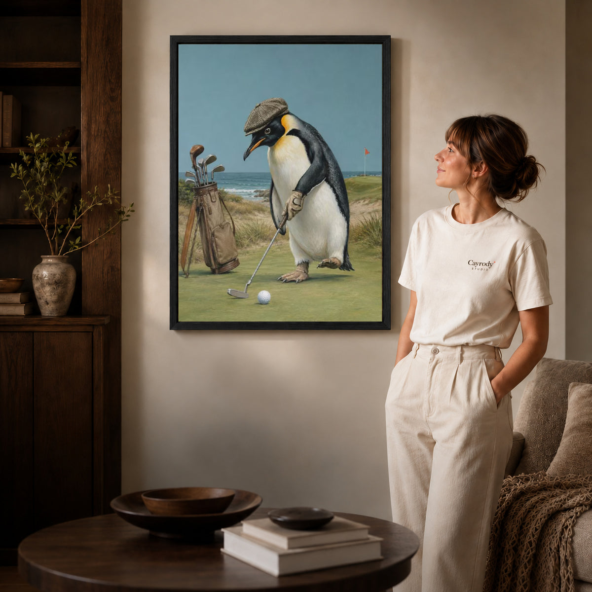 Golf Penguin Canvas Art inside a black frame in a softly lit living room with books.
