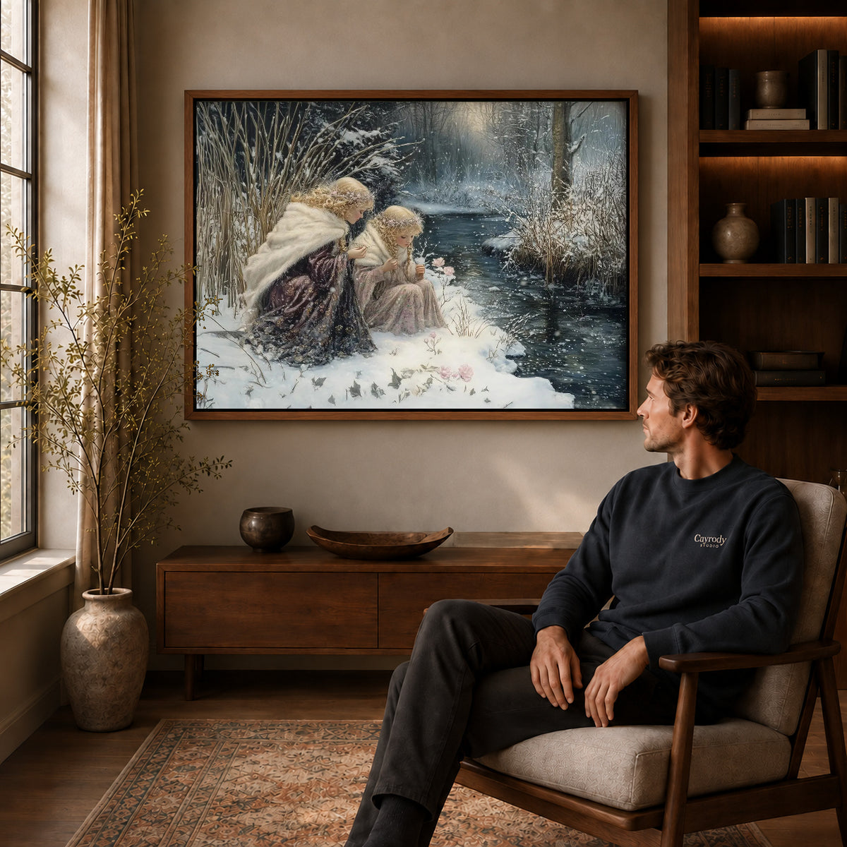 Winter Sisters Canvas Art displayed in a walnut frame above wooden furniture beside a seated man.