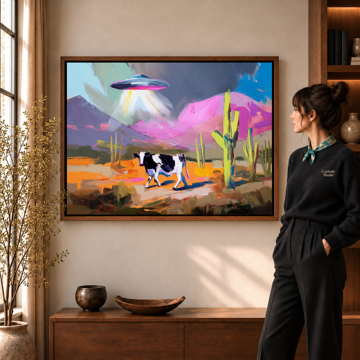 UFO Cow Canvas Art in a walnut frame beside a standing woman and warm wooden furniture.