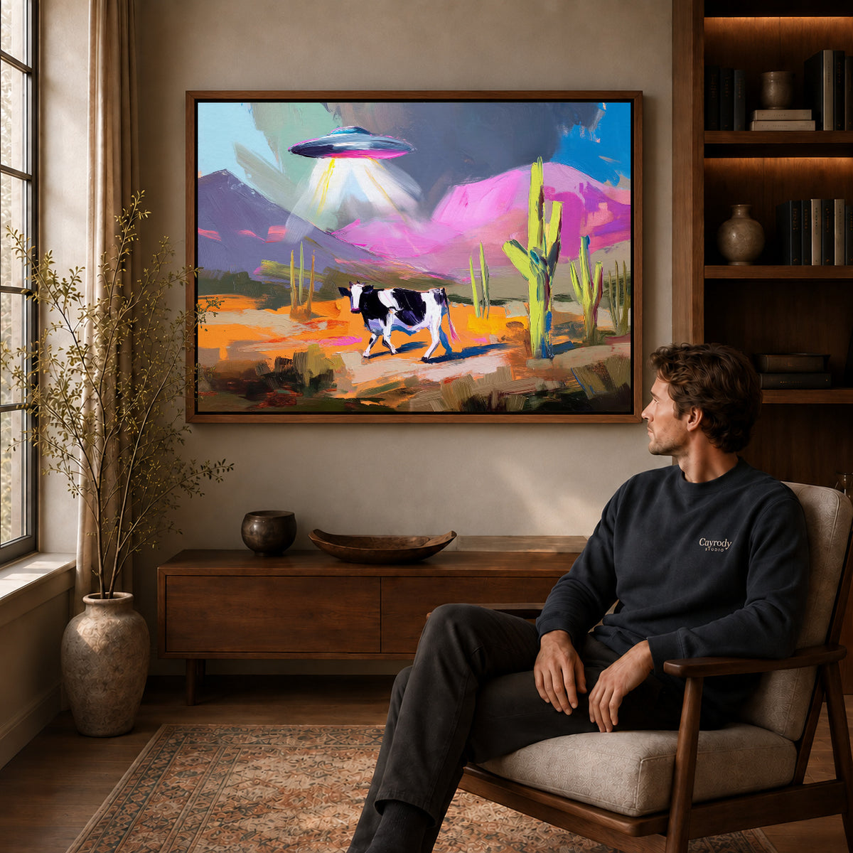UFO Cow Canvas Art displayed in a walnut frame above wooden furniture beside a seated man.