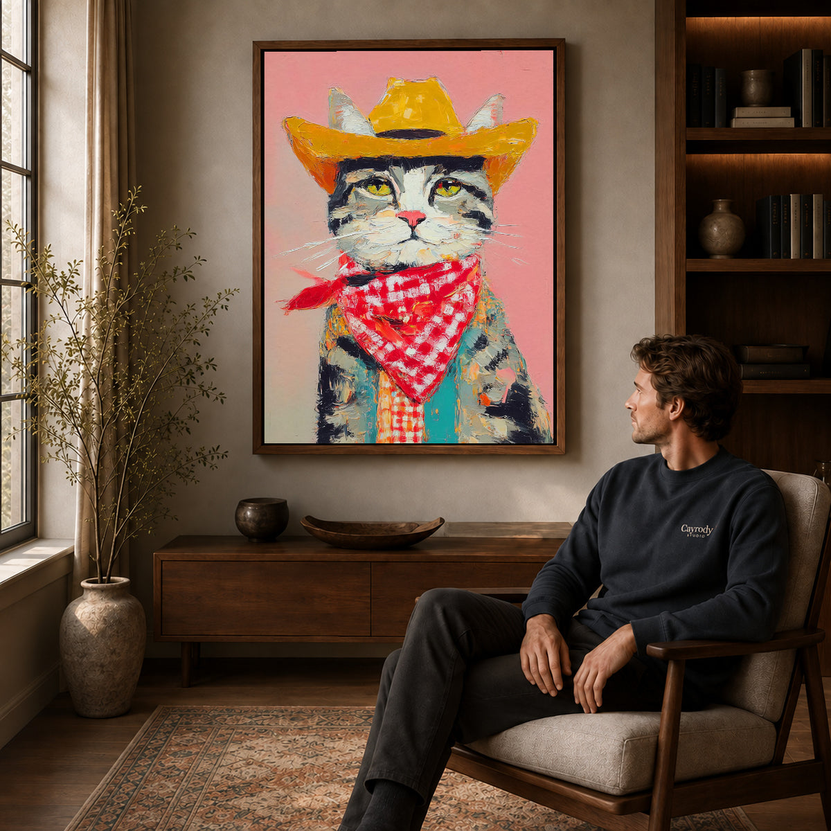 Cowboy Cat Canvas Art displayed in a walnut frame above wooden furniture beside a seated man.