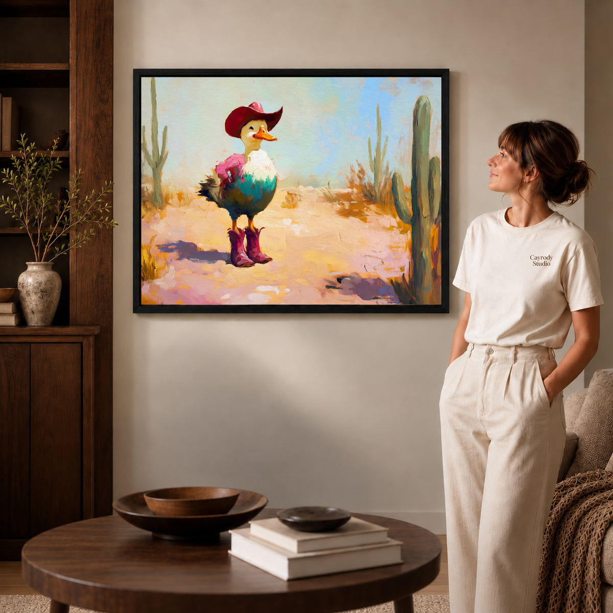 Black framed cowboy duck canvas art displayed beside a woman with natural light across the wall.