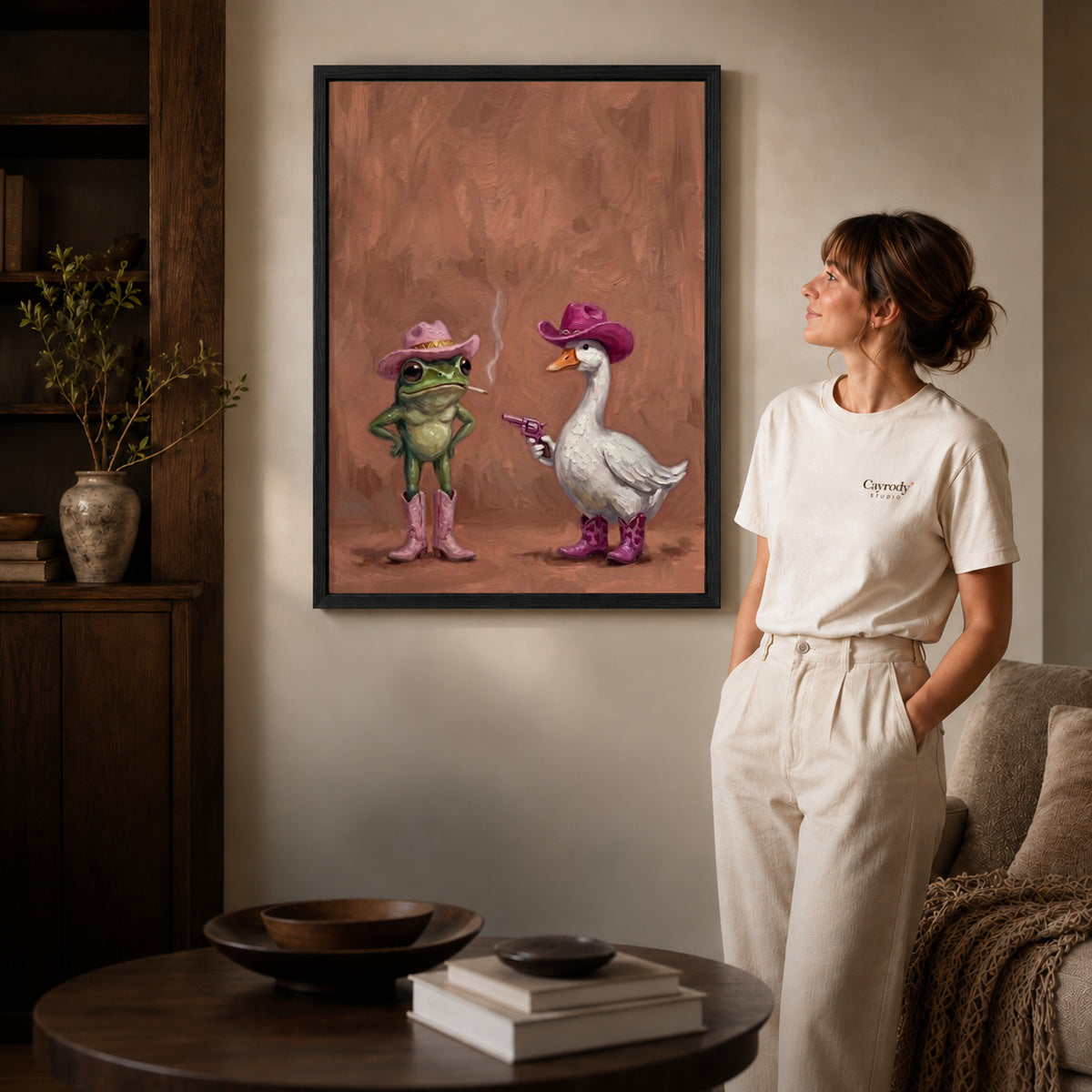 Black framed frog goose canvas art displayed beside a woman with natural light across the wall.