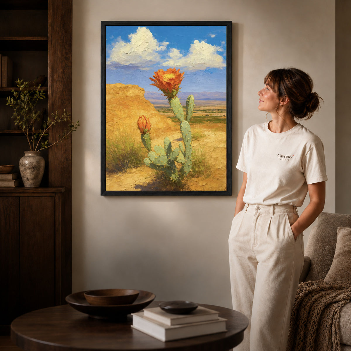 Cactus Canvas Art inside a black frame in a softly lit living room with books.