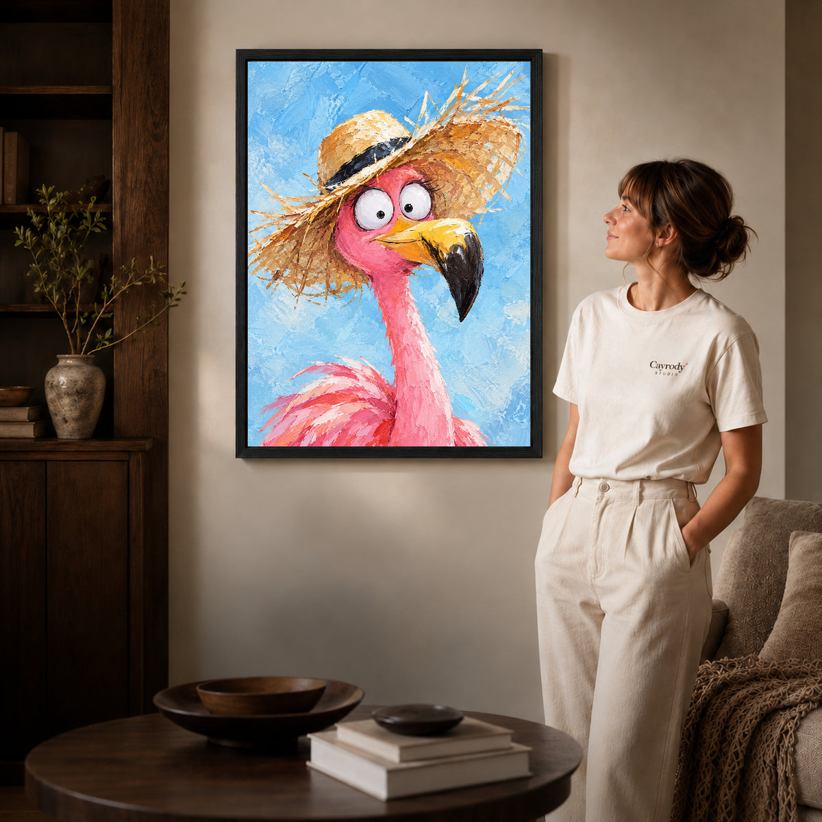 Black framed flamingo canvas art displayed beside a woman with natural light across the wall.