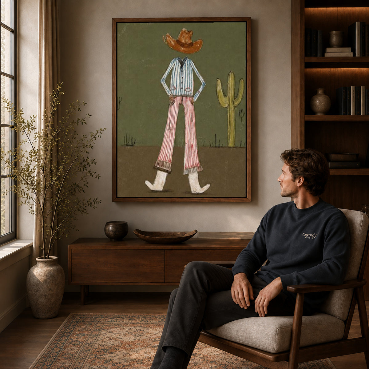Cowboy Canvas Wall Art displayed in a walnut frame above wooden furniture beside a seated man.