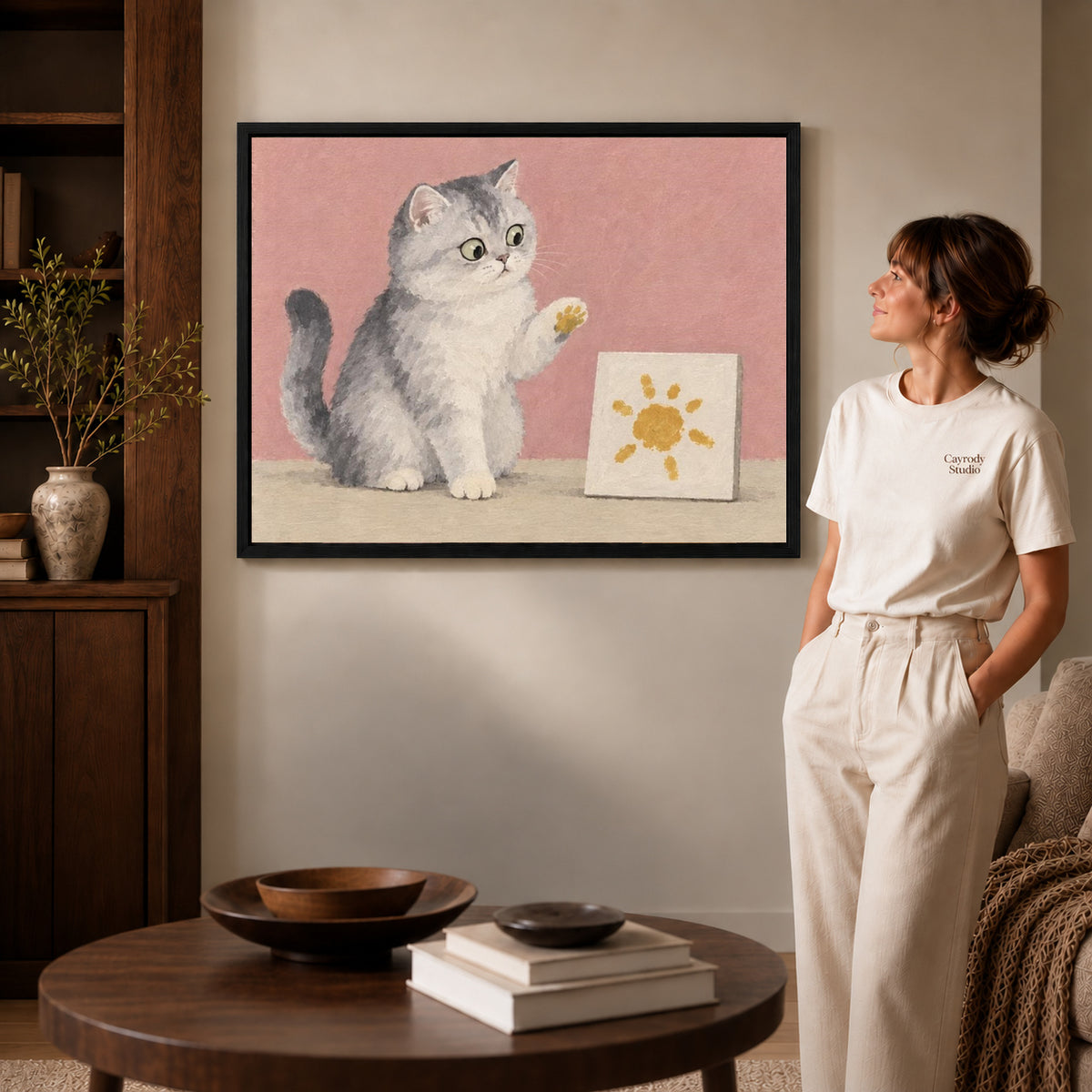 Artist Cat Canvas Art inside a black frame in a softly lit living room with books.