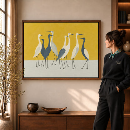 Heron Canvas Wall Art in a walnut frame beside a standing woman and warm wooden furniture.