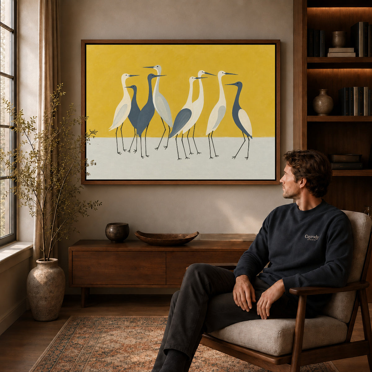 Heron Canvas Wall Art displayed in a walnut frame above wooden furniture beside a seated man.