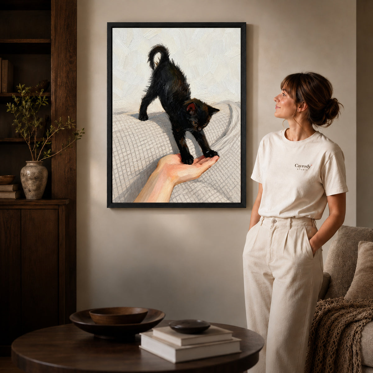 Black Kitten Canvas Art inside a black frame in a softly lit living room with books.