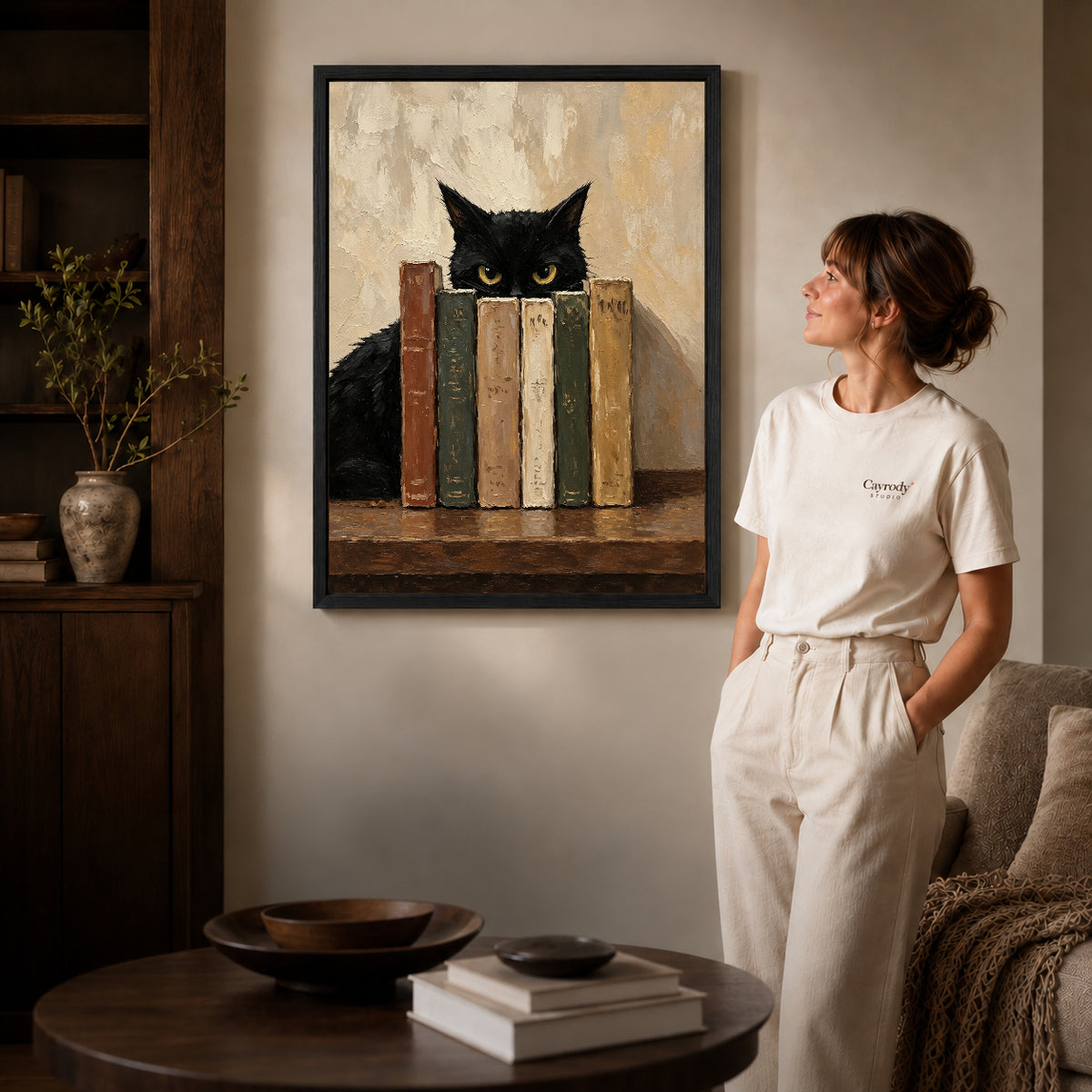 Bookish Cat Canvas Art inside a black frame in a softly lit living room with books.