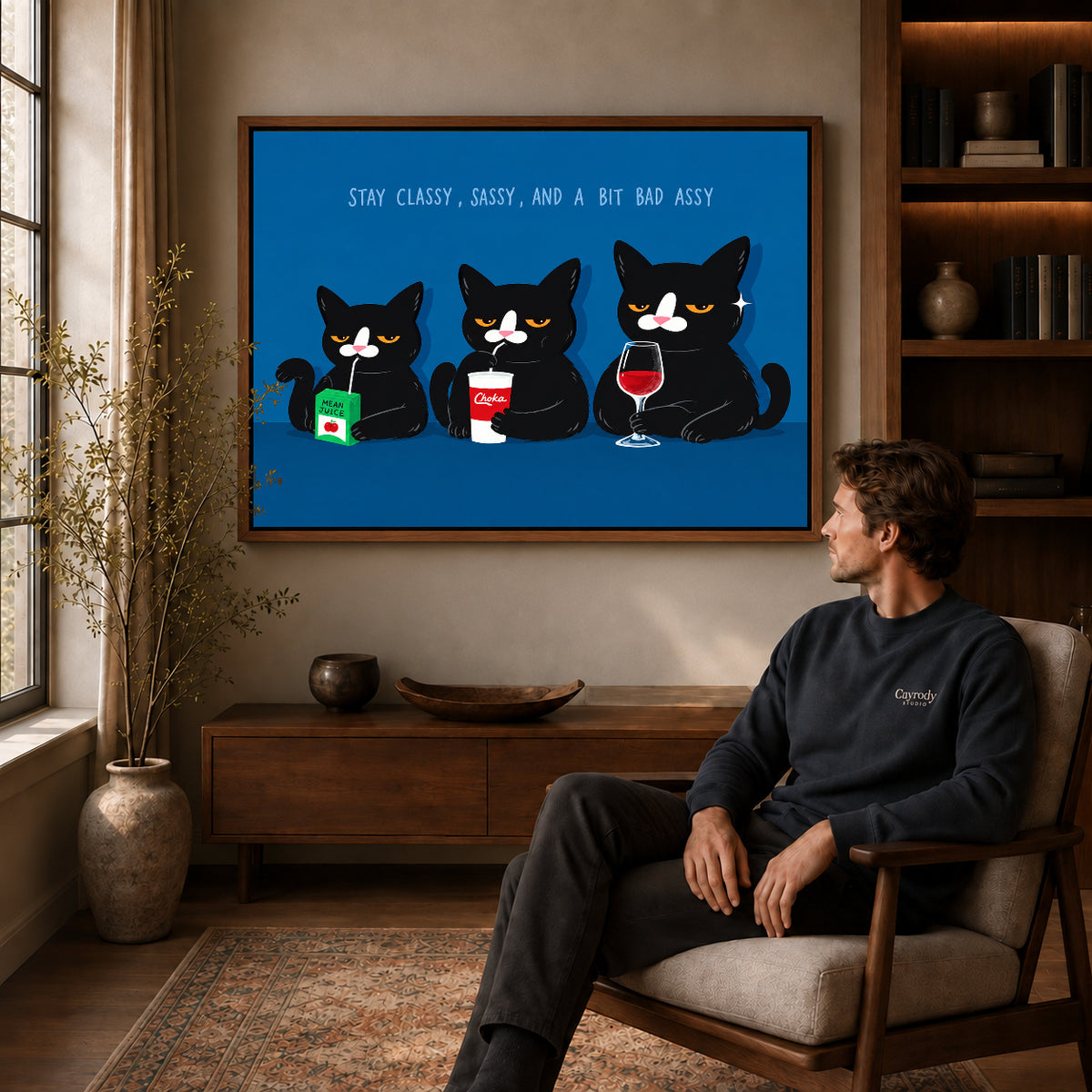 Sassy Cat Trio Canvas Art displayed in a walnut frame above wooden furniture beside a seated man.