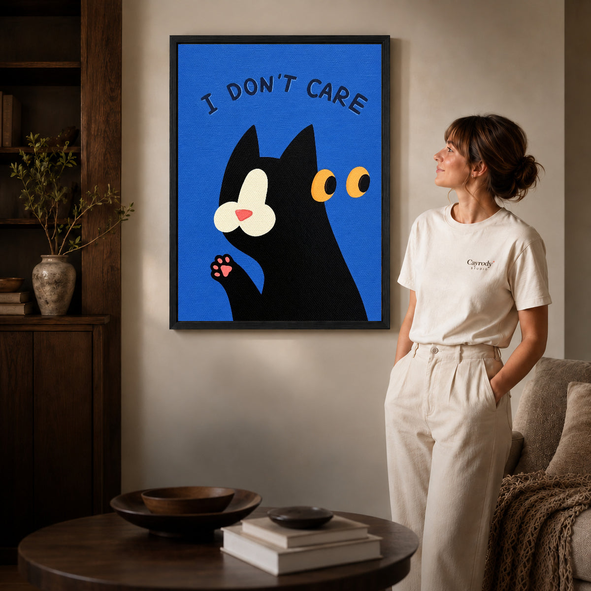 Black framed unbothered cat canvas art displayed beside a woman with natural light across the wall.