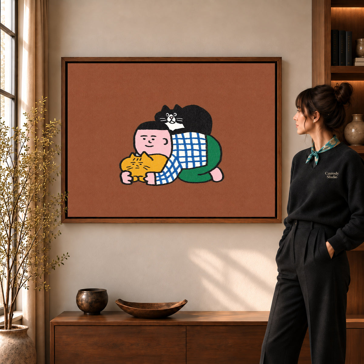 Cuddling Cats Canvas Art in a walnut frame beside a standing woman and warm wooden furniture.