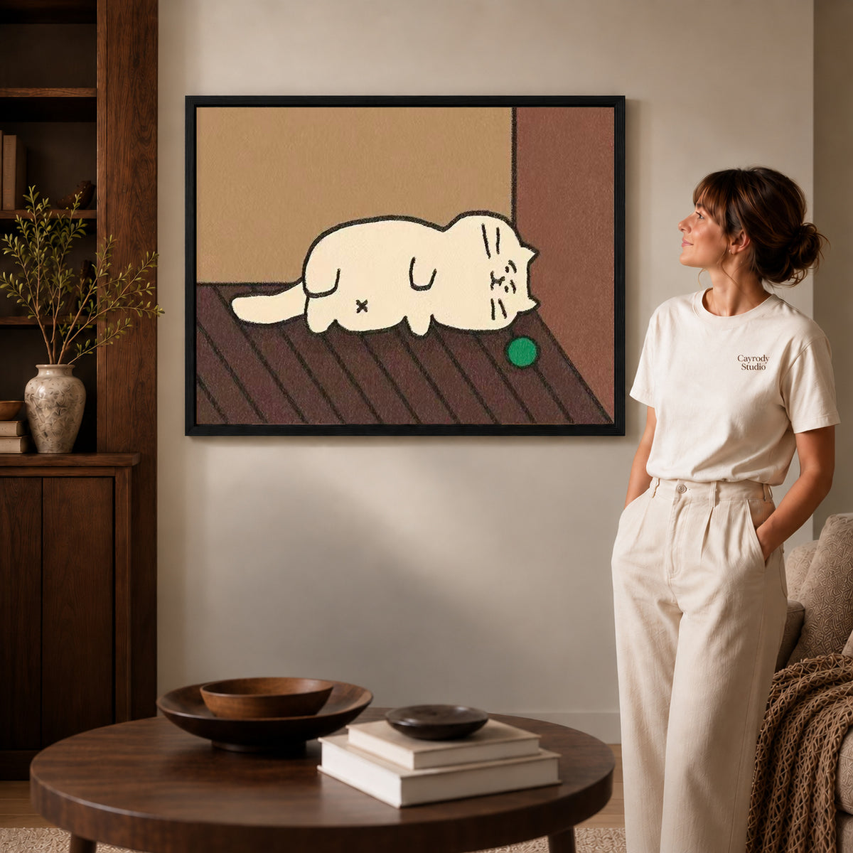 Sleepy Cat Canvas Art inside a black frame in a softly lit living room with books.