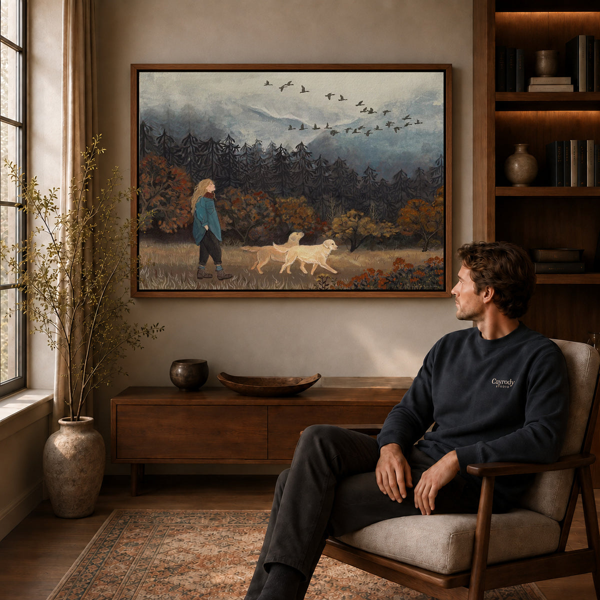 Autumn Dog Walk Canvas Art displayed in a walnut frame above wooden furniture beside a seated man.