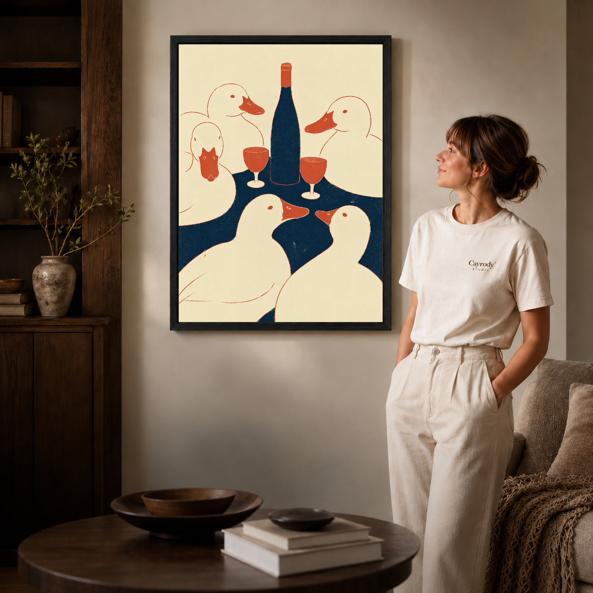 Ducks Toast Canvas Art inside a black frame in a softly lit living room with books.