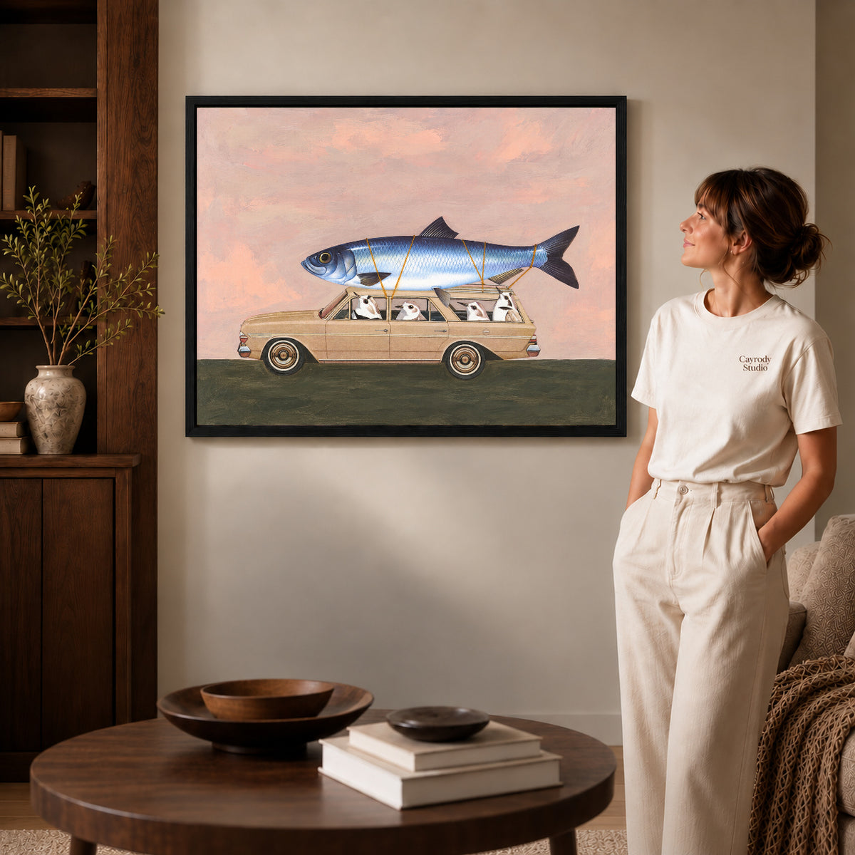 Black framed fishing trip canvas art displayed beside a woman with natural light across the wall.
