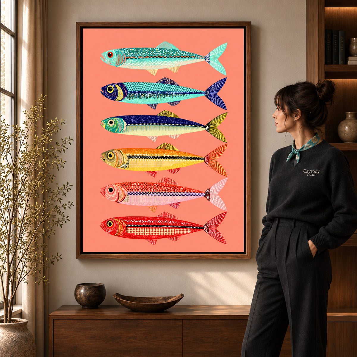 Colorful Sardine Canvas Art in a walnut frame beside a standing woman and warm wooden furniture.