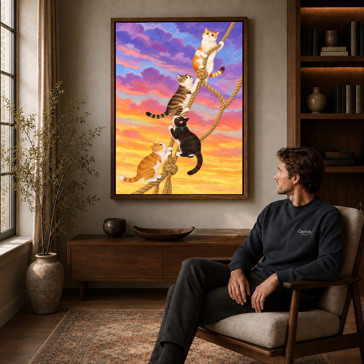 Walnut framed whimsical climbing cats canvas art above a seated man in a cozy wood furnished living room.