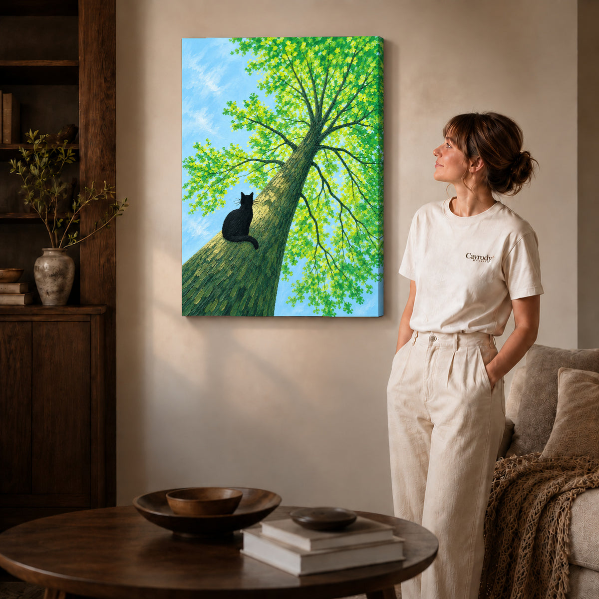 Gallery wrapped black cat tree canvas art with subtly shaded canvas edges beside a woman wearing cream clothing.