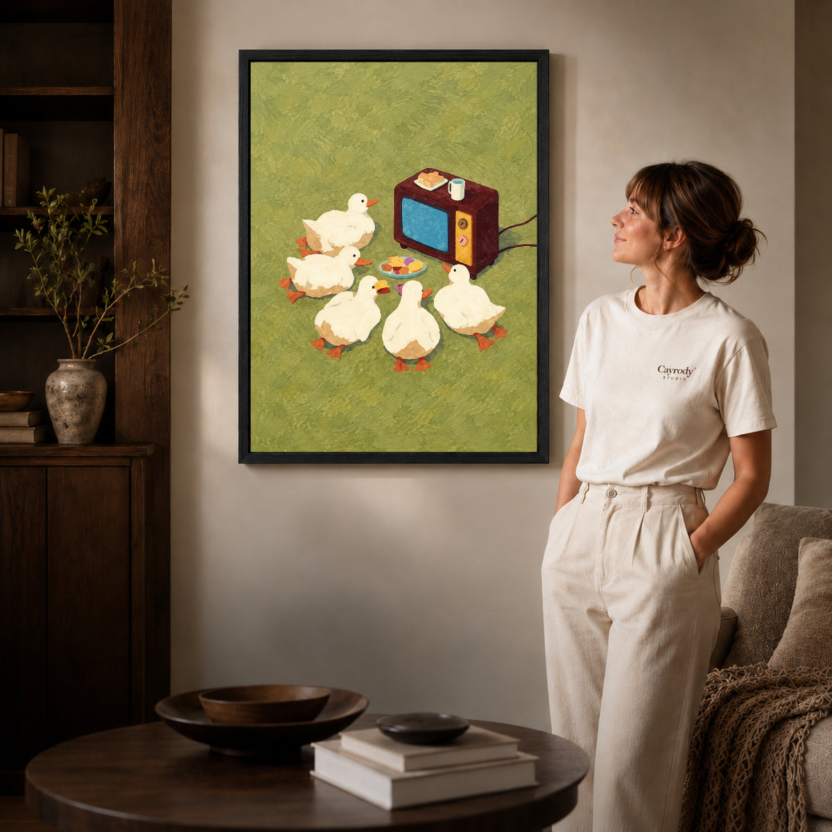 Black framed funny duck television canvas art displayed beside a woman in a warm wood living room.
