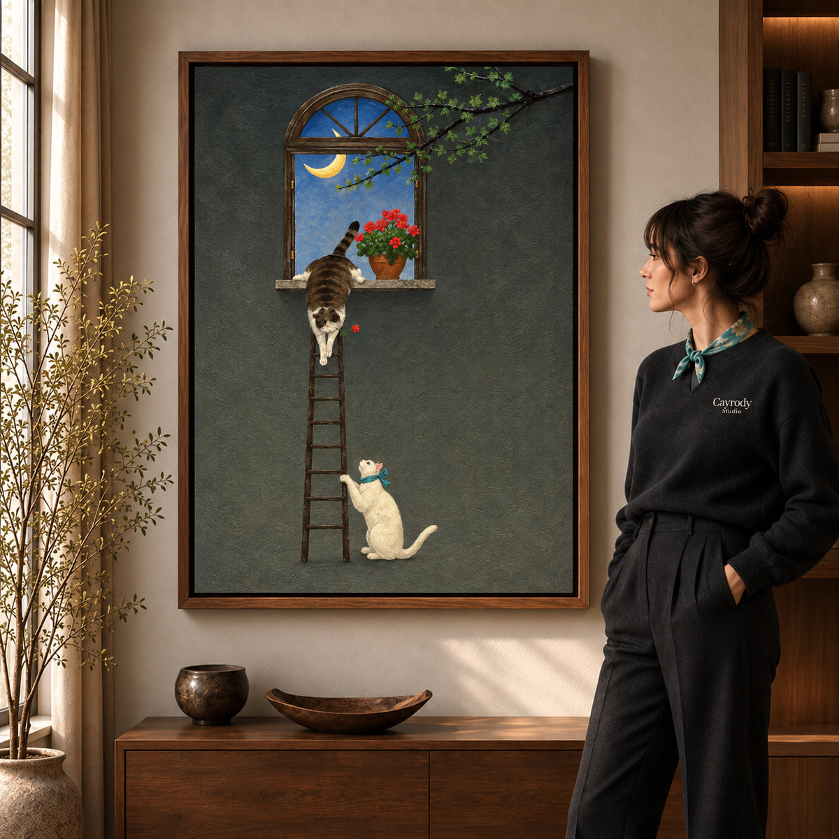 Moonlit ladder cats canvas art in a walnut frame beside a woman in a warm living room.