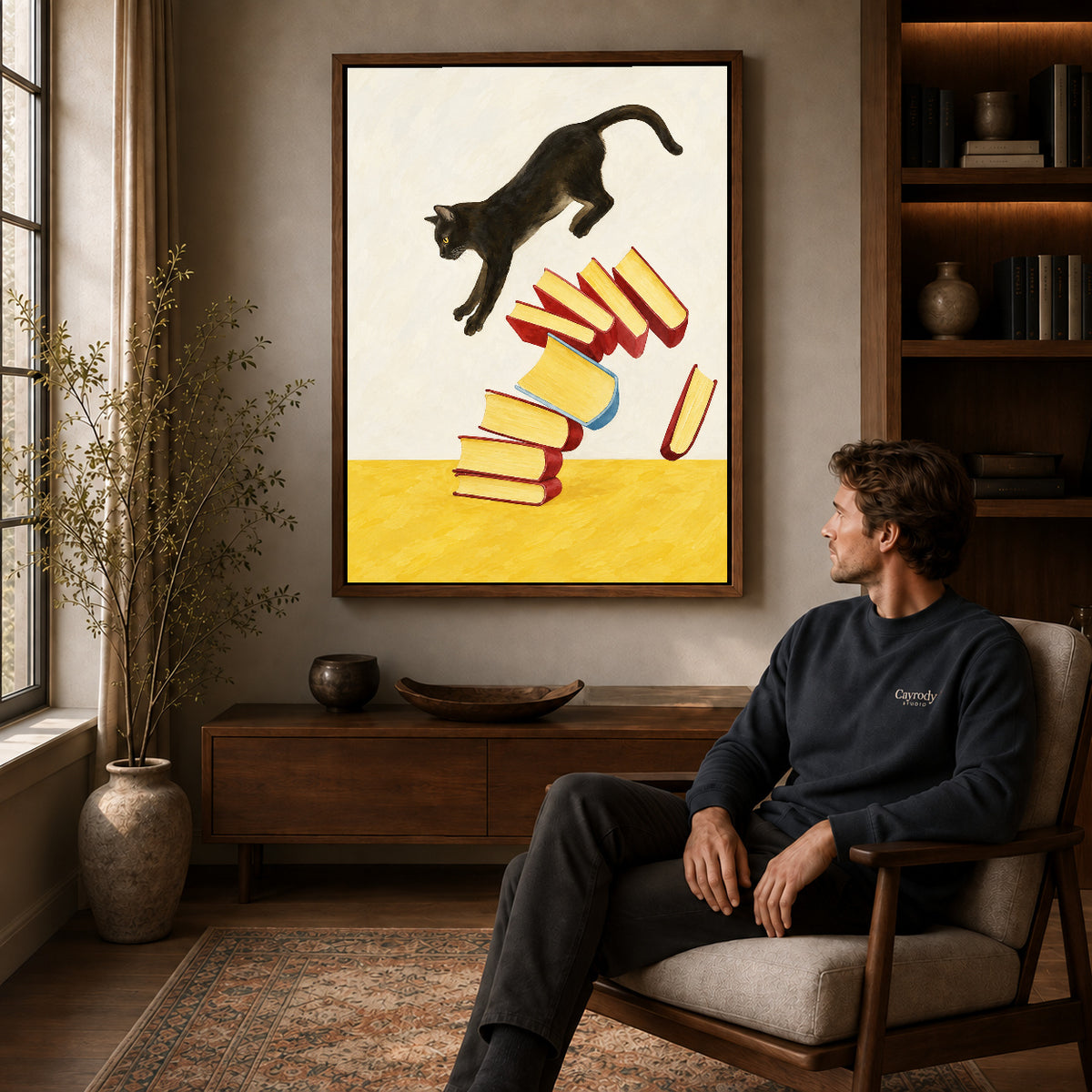 Walnut framed leaping cat books canvas art above a seated man in a cozy wood furnished living room.
