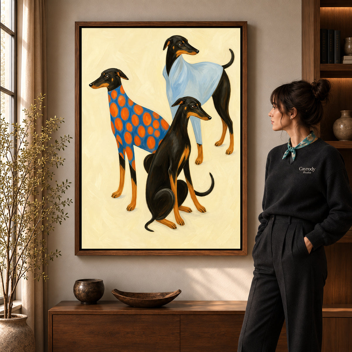 Stylish greyhound trio canvas art in a walnut frame beside a woman in a warm living room.
