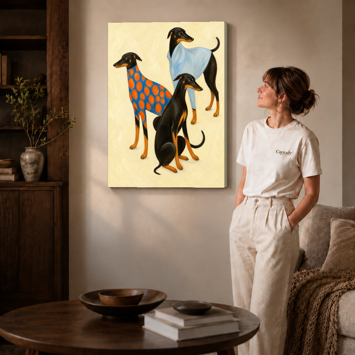 Gallery wrapped stylish greyhound trio canvas art with subtly shaded canvas edges beside a woman wearing cream clothing.