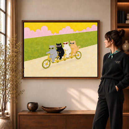 Tandem cycling cats canvas art in a walnut frame beside a woman in a warm living room.