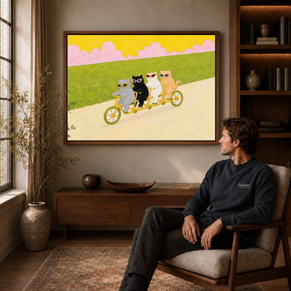 Walnut framed landscape tandem cycling cats canvas art above a seated man in a cozy wood furnished living room.