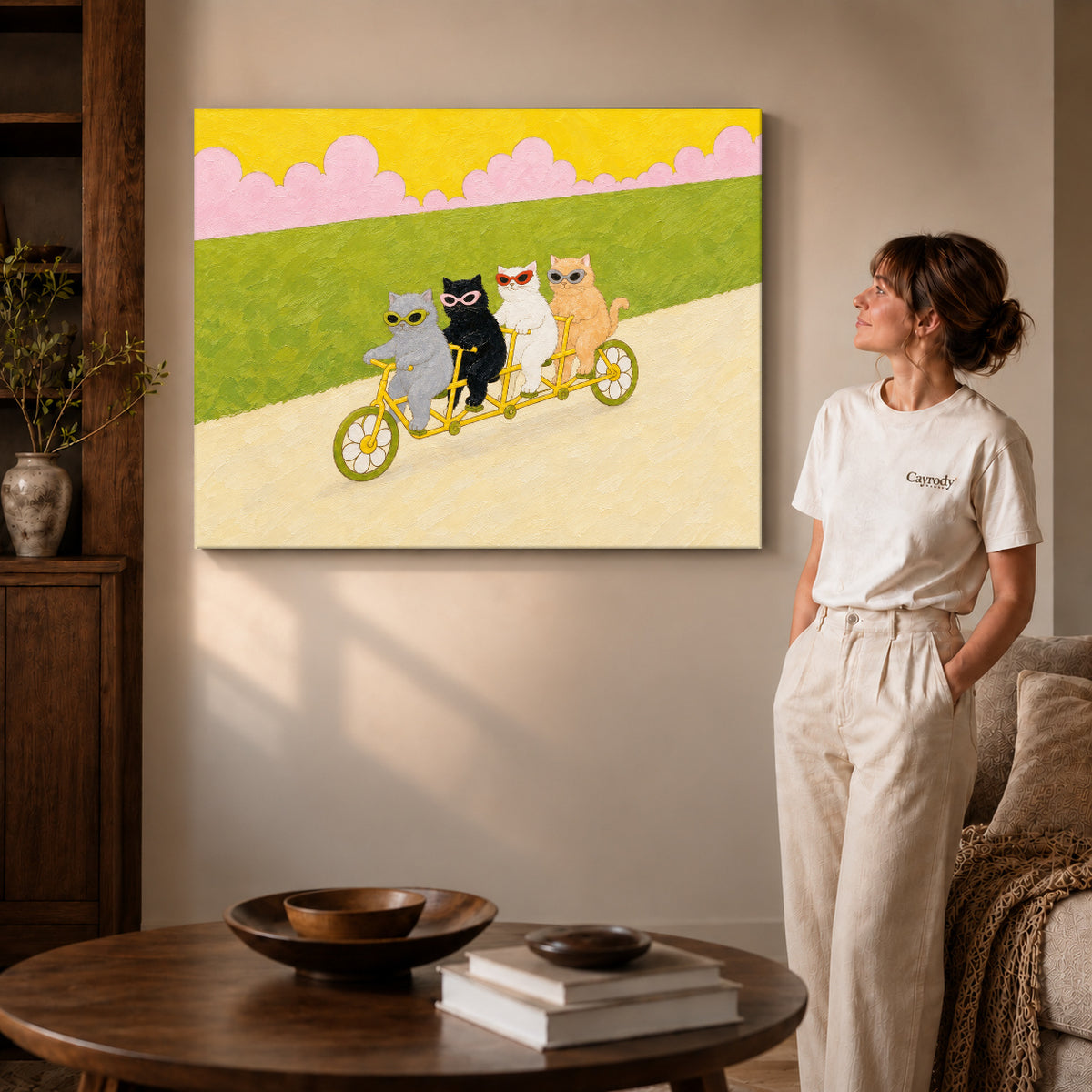 Gallery wrapped landscape tandem cycling cats canvas art with subtly shaded canvas edges beside a woman wearing cream clothing.
