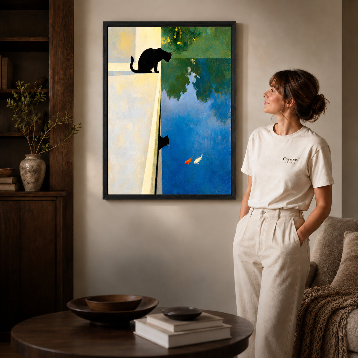 Black framed reflective black cat canvas art displayed beside a woman in a warm wood living room.