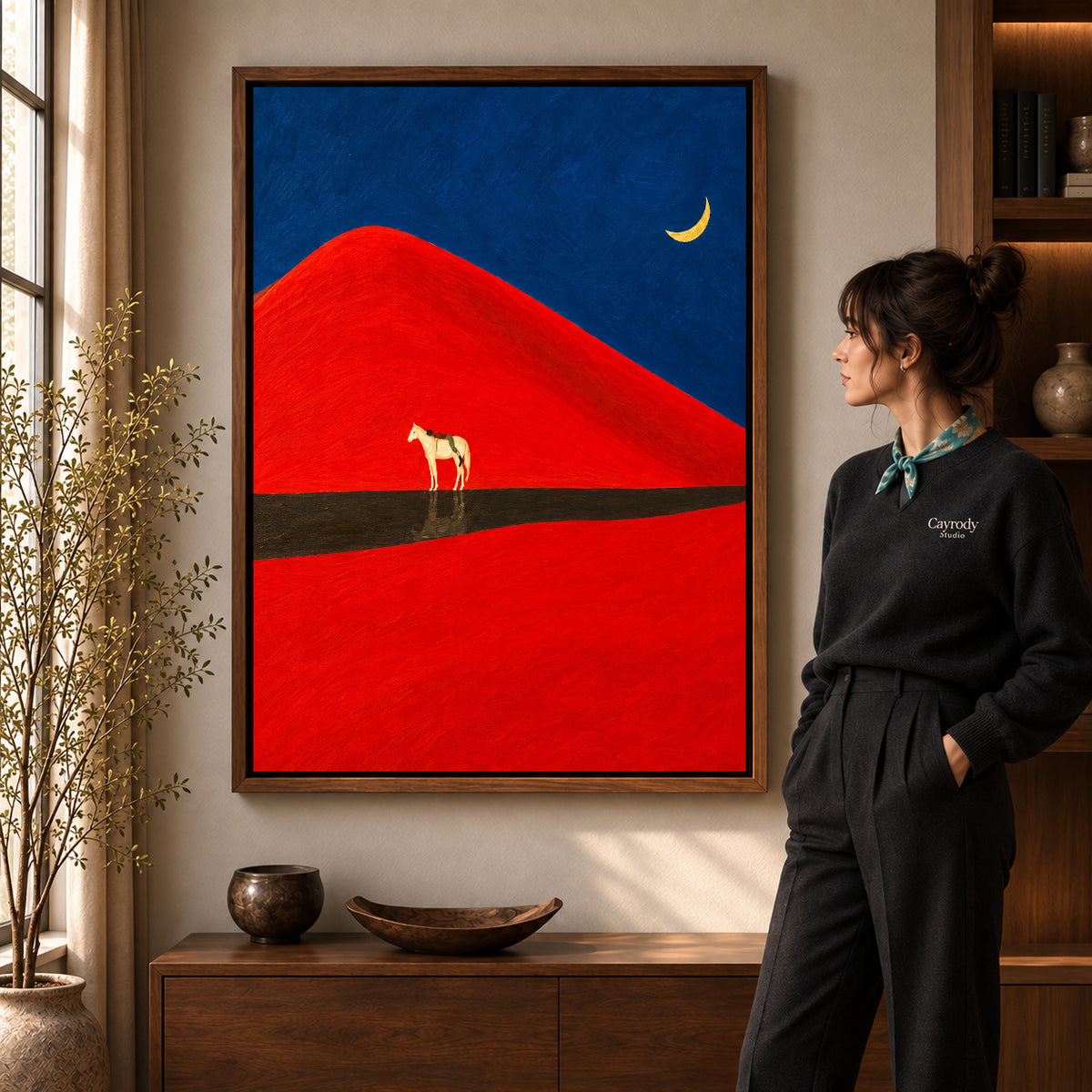 Red dune horse canvas art in a walnut frame beside a woman in a warm living room.