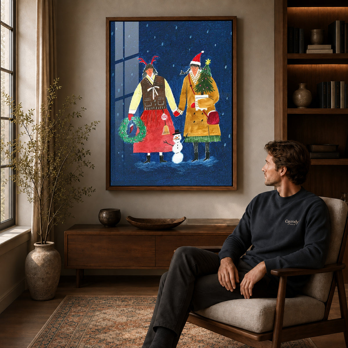 Folk Christmas canvas art in a walnut frame above a console beside a seated man.
