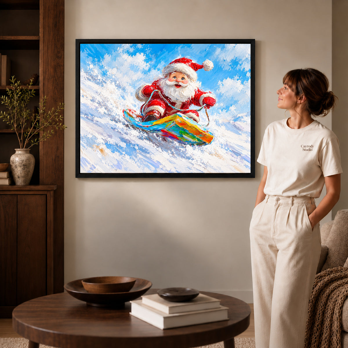 Snowboard Santa canvas art in a black frame beside a woman and round wooden table.
