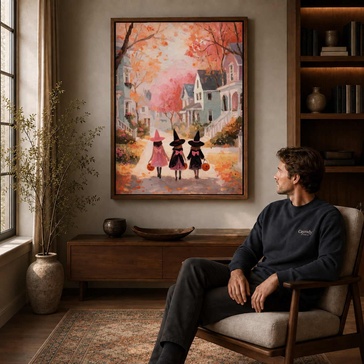 Little witches canvas art in a walnut frame above a console beside a seated man.
