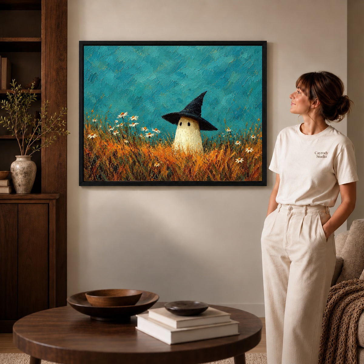 Meadow ghost canvas art in a black frame beside a woman and round wooden table.