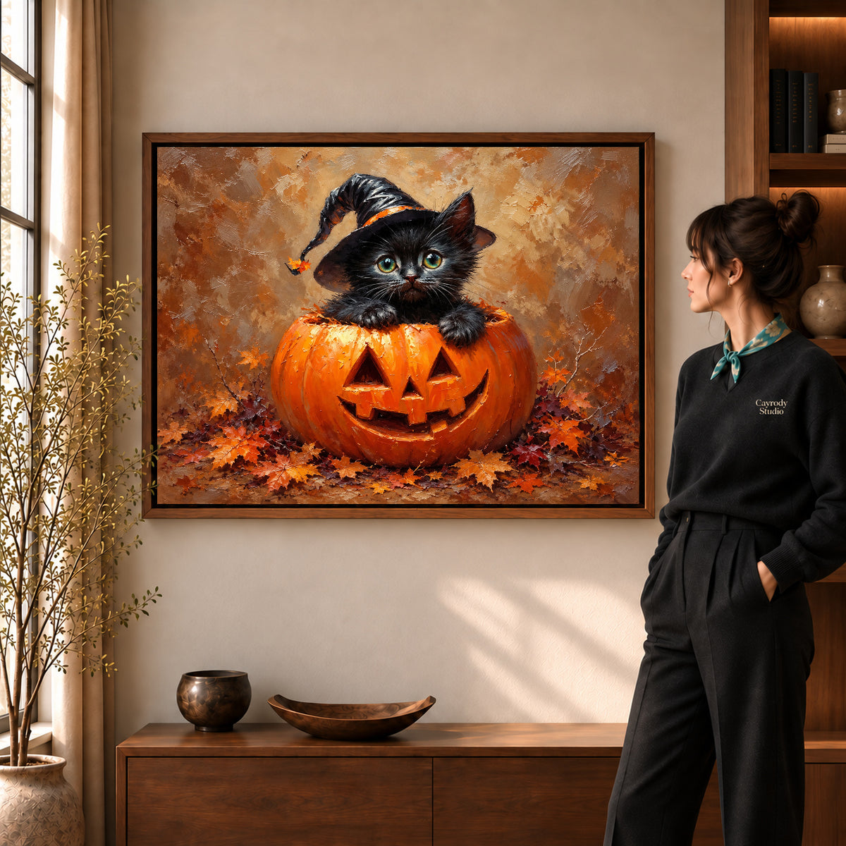 Pumpkin kitten canvas art in a walnut frame beside a standing woman and wooden console.